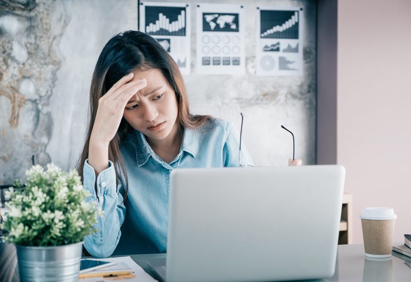 A woman with her hand on her forehead looking confused and frustrated at her laptop.