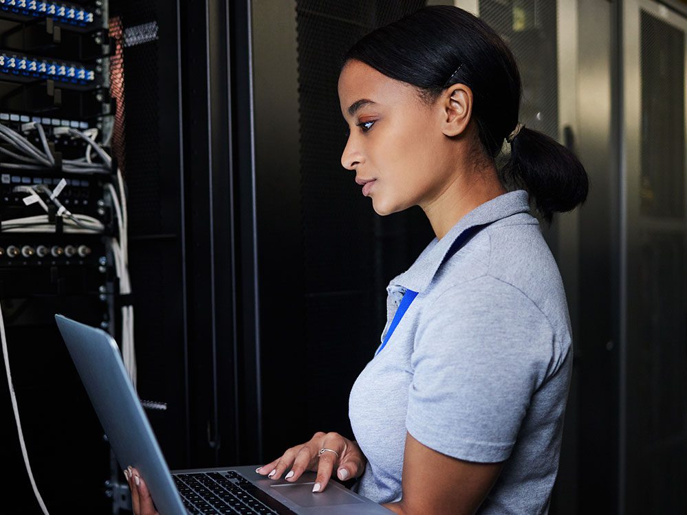 Engineer, laptop database and woman in server room for software update or maintenance at night. Cybersecurity coder, cloud computing and female programmer with computer for networking in data