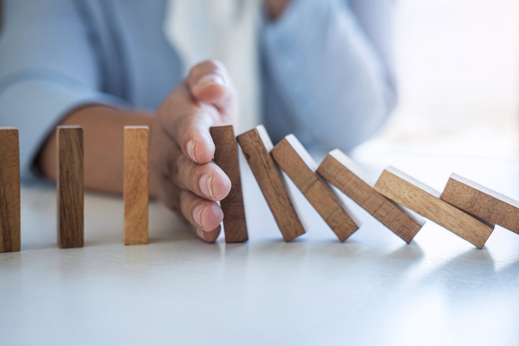 A series of wooden dominoes set up in a chain, with a hand blocking them from falling over.