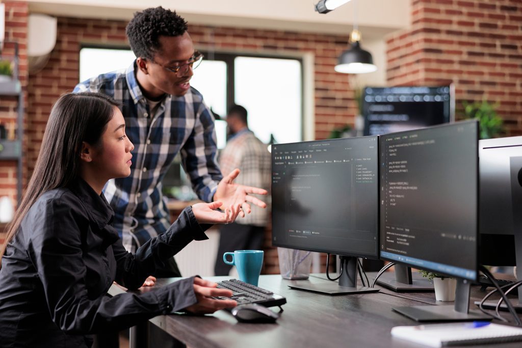 A pair of IT experts working in an office and looking at a pair of screens