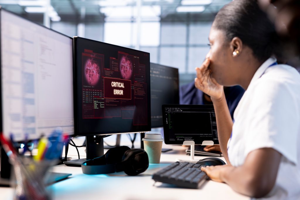 A woman at her desk with multiple monitors, the center of which displays "Critical Error" in red.